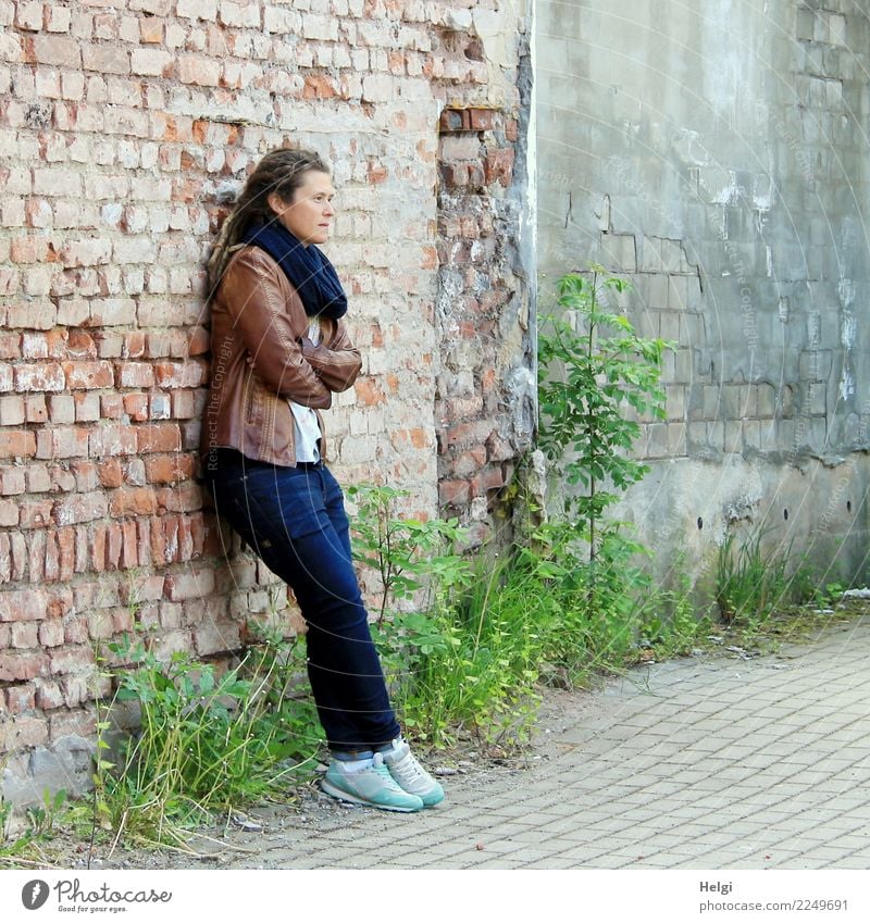 nachdenkliche Frau mit Dreadlocks, in Jeans und brauner Lederjacke steht an einer alten verfallenen Häuserwand Mensch feminin Erwachsene 1 30-45 Jahre Umwelt