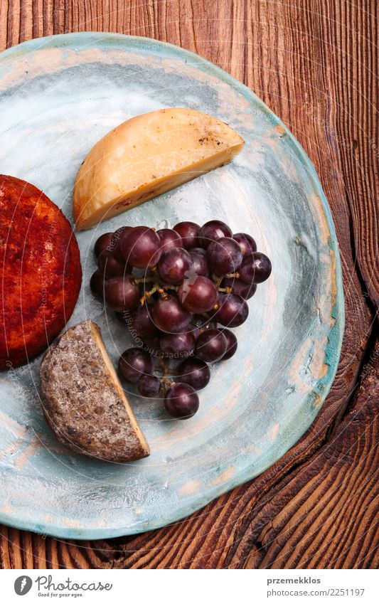 Käse und schwarze Trauben auf handgemachter blauer Tonplatte Lebensmittel Frucht Frühstück Teller Tisch Holz Rost frisch lecker oben Keramik Essen zubereiten