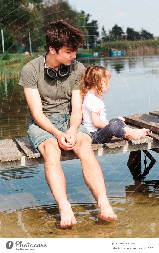 Junge und seine kleine Schwester sitzen auf einem Steg über dem See und tauchen an sonnigen Sommertagen die Füße ins Wasser Lifestyle Freude Glück Erholung