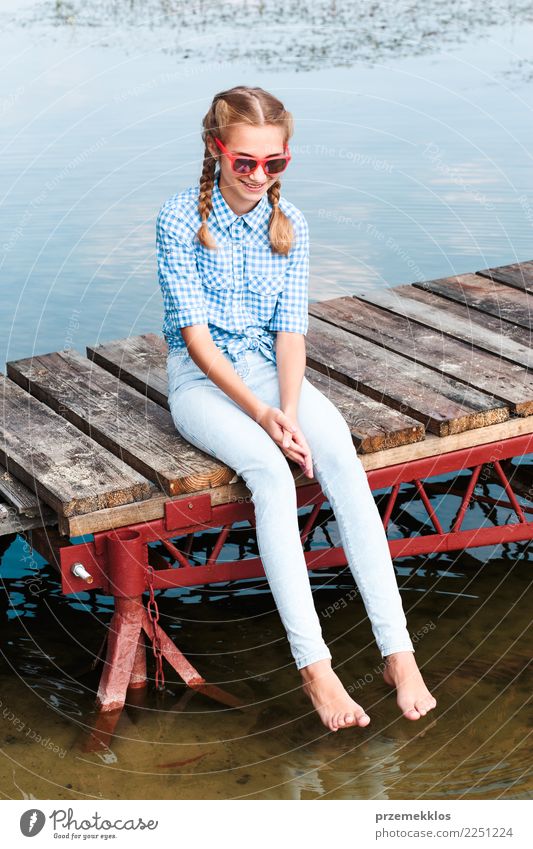 Mädchen, das auf Anlegestelle über dem See sitzt und Füße im Wasser eintaucht Lifestyle Freude Glück Erholung Freizeit & Hobby Ferien & Urlaub & Reisen Sommer