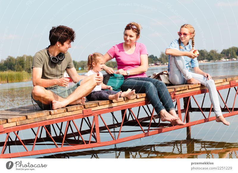 Eine Familie, die gemeinsam Urlaub macht und an einem sonnigen Sommertag einen Imbiss am Steg über dem See einnimmt Freude Glück Erholung Freizeit & Hobby