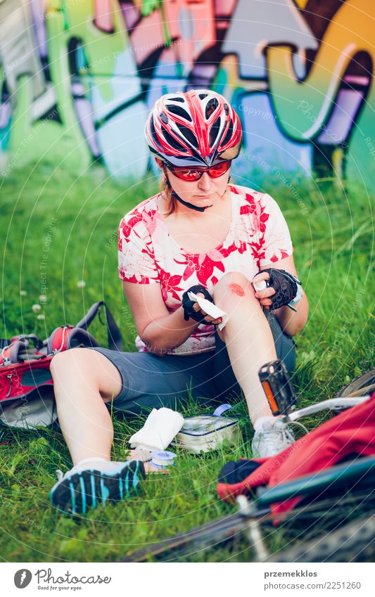 Frau, die die Wunde auf ihrem Knie mit Medizin im Spray ankleidet Lifestyle Ferien & Urlaub & Reisen Sommer Sport Fahrradfahren Mensch Erwachsene Gras Schmerz