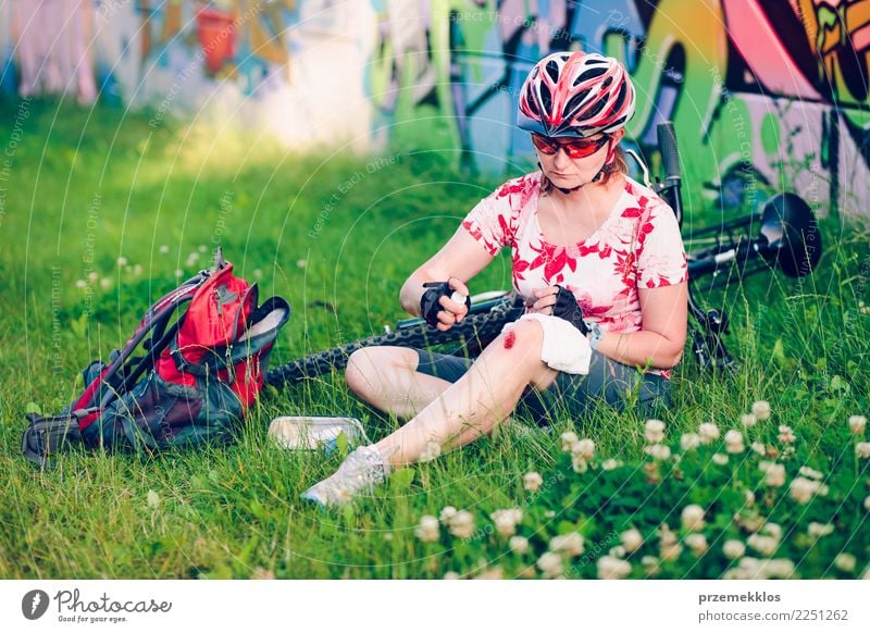 Frau, die die Wunde auf ihrem Knie mit Medizin im Spray ankleidet Lifestyle Ferien & Urlaub & Reisen Sommer Sport Fahrradfahren Mensch Erwachsene sitzen Unfall