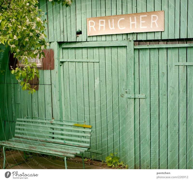 Gesundheitsschutz. Mintgrüne bank vor mintgrüner Holzhütte mit pappschild Raucher. Raucherecke Mauer Wand Bank Blüte Baum Schilder & Markierungen