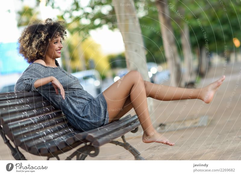 Frau mit Afro-Frisur, die auf einer Bank sitzt und ihre Beine bewegt. Lifestyle Stil Glück schön Haare & Frisuren Gesicht Mensch feminin Junge Frau Jugendliche