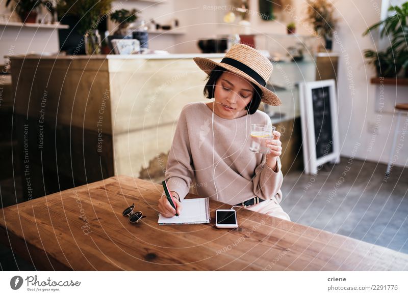 Asiatische Schreibensanmerkungen der jungen Frau im Notizbuch trinken Tisch Musik Arbeit & Erwerbstätigkeit Erwachsene Jugendliche Musiknoten Hut Papier