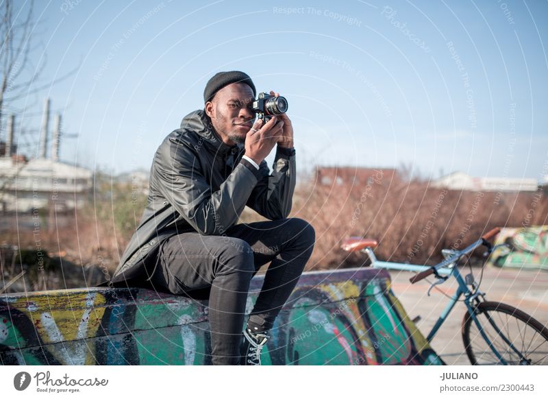 Junger moderner Mann, der auf der Halfpipe sitzt und mit der Kamera fotografiert. Stadt Stadtleben Großstadt Fotokamera Schlittschuhlaufen Skateplatz Lifestyle