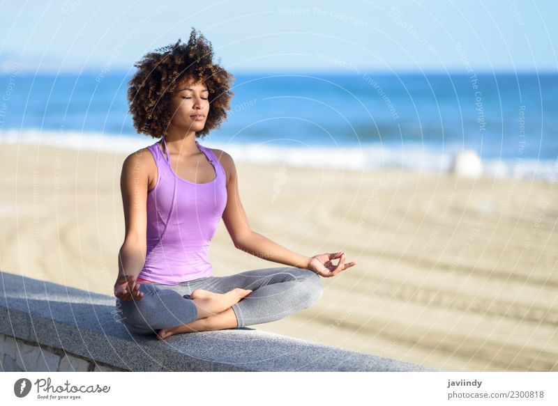Schwarze Frau mit Afrofrisur, die am Strand mit geschlossenen Augen Yoga-Asanas macht. Lifestyle Haare & Frisuren Wellness Erholung Meditation Freizeit & Hobby