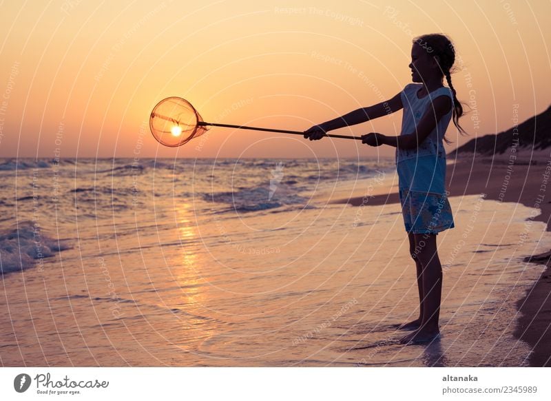 Ein glückliches kleines Mädchen, das zur Sonnenuntergangszeit am Strand spielt. Lifestyle Freude Glück schön Erholung Freizeit & Hobby Spielen