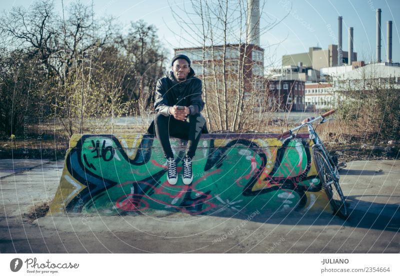 Der junge moderne Hipster sitzt auf einer Halfpipe im Skatepark. Stadt Stadtleben Großstadt Fotokamera Schlittschuhlaufen Skateplatz Lifestyle Schickimicki