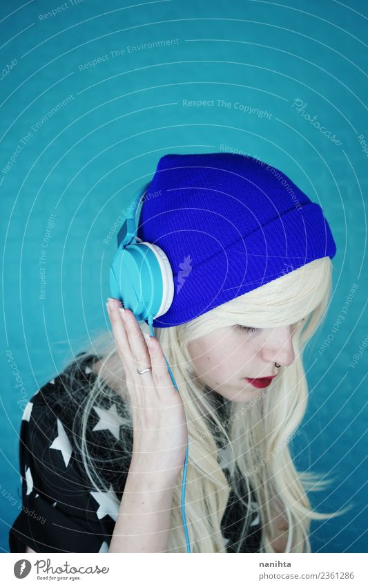 Junge blonde Frau beim Musikhören vor blauem Hintergrund Lifestyle Stil Design Haare & Frisuren Freizeit & Hobby Headset Technik & Technologie
