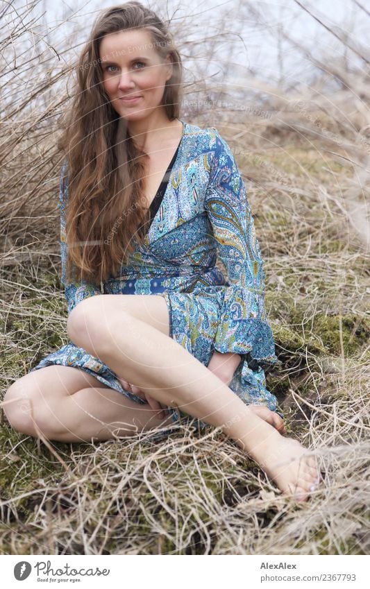 jungen Frau in Sommerkleid sitzt zwischen Büschen und Gras barfuß in der Natur Lifestyle Freude schön Körper Leben harmonisch Ausflug Abenteuer Junge Frau