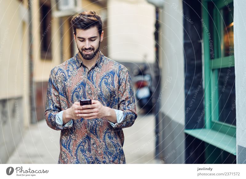 Junger lächelnder Mann schaut auf sein Smartphone im Freien. Lifestyle Stil schön Haare & Frisuren Telefon PDA Mensch Junger Mann Jugendliche Erwachsene 1