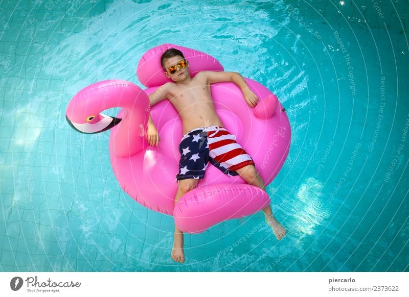 Kleiner Junge auf einem aufblasbaren Flamingo in einem Schwimmbad. Lifestyle Freude Erholung Freizeit & Hobby Ferien & Urlaub & Reisen Sommer Sonne Sonnenbad
