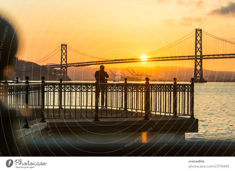 # 750 Oakland Bay Bridge San Francisco Hafen Meer Sonnenaufgang Anlegestelle Mann Fotograf Brücke ruhig Gegenlicht Farbfoto orange Licht Hängebrücke Einsamkeit