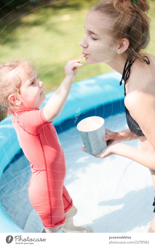 Teenager-Mädchen mit ihrer kleinen Schwester verbringen Zeit zusammen im Schwimmbad in einem Garten genießen Eis essen an einem sonnigen Sommertag. Familie Qualität Zeit