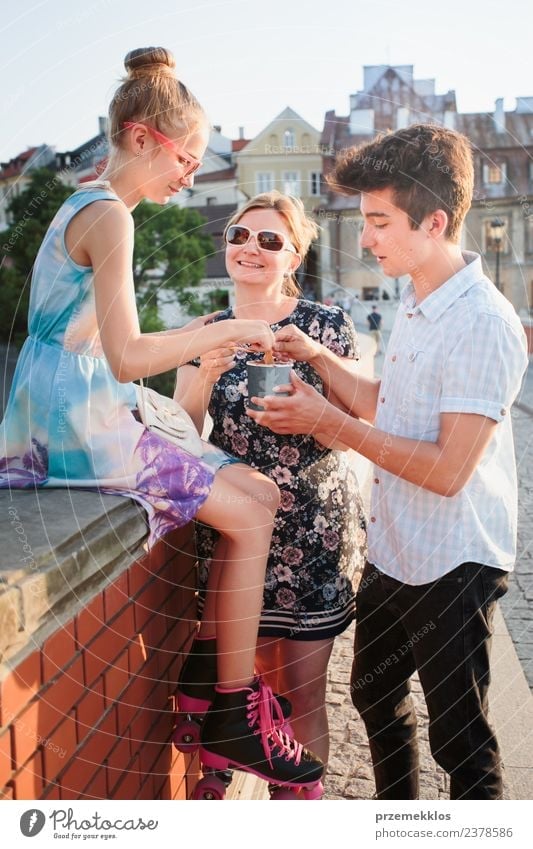 Familien, die im Stadtzentrum Zeit miteinander verbringen, genießen es, an einem Sommertag Eiscreme zu essen. Mutter, Teenager, Mädchen und Junge verbringen an sonnigen Nachmittagen viel Zeit miteinander und essen ein süßes Dessert. Stadtzentrum, Altstadt im Hintergrund