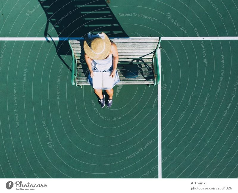 Eine Luftaufnahme der jungen Frau, die ein Buch liest. Fluggerät Tasche lesen Leser Hut Bank Schatten Dröhnen Tennisplatz Außenaufnahme Sonnenuntergang Sommer