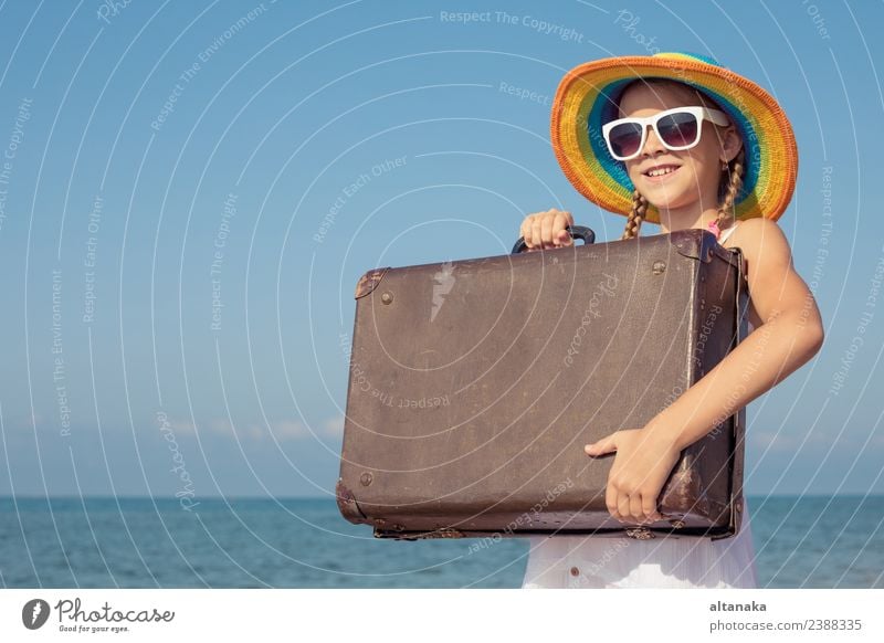 Ein glückliches kleines Mädchen mit Koffer, das am Strand steht. Lifestyle Freude Glück Erholung Freizeit & Hobby Spielen Ferien & Urlaub & Reisen Tourismus
