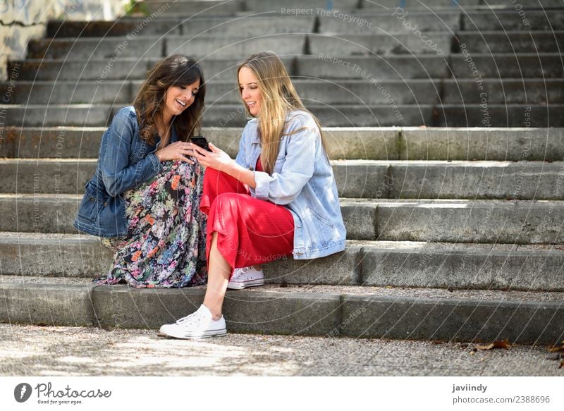 Zwei junge Frauen, die sich ein Smartphone im Freien ansehen. Lifestyle kaufen Freude Glück schön Telefon PDA Technik & Technologie Mensch feminin Junge Frau