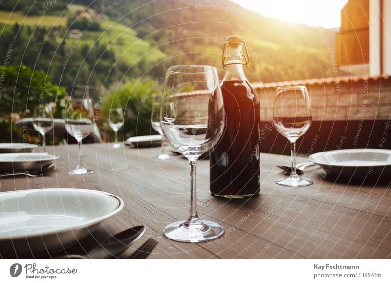 Flasche Rotwein und gedeckter Tisch auf der Veranda Festessen Getränk Alkohol Wein Geschirr Teller Glas Gabel Löffel Lifestyle Reichtum elegant Stil Leben