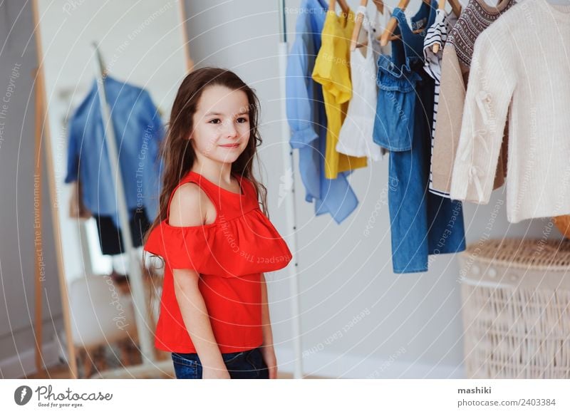 süßes kleines Kind Mädchen bei der Auswahl neuer Kleidung kaufen Stil Mode Bekleidung Sammlung Lächeln hell trendy modern rot Farbe Outfit viele wählen anhaben