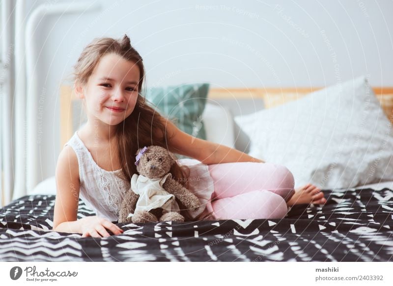süßes glückliches Kind Mädchen entspannend zu Hause auf dem Bett Lifestyle Freude Erholung Spielzeug Teddybär Lächeln schlafen träumen klein lustig niedlich