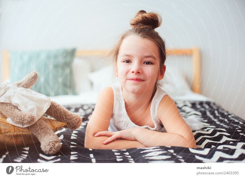 fröhliches kleines Kind Mädchen, das morgens auf ihrem Bett liegt. Lifestyle Freude Glück Haare & Frisuren Erholung Sonne Schlafzimmer Spielzeug Teddybär