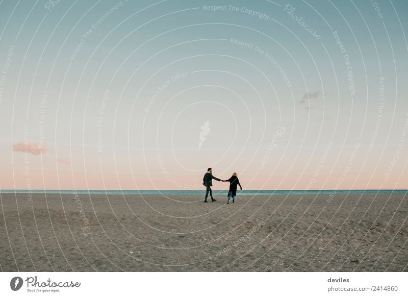 Junges Paar, das in der Abenddämmerung an einem einsamen Strand mit dem Meer im Hintergrund auf dem Sand spazieren geht. Lifestyle Winter Mensch Junge Frau