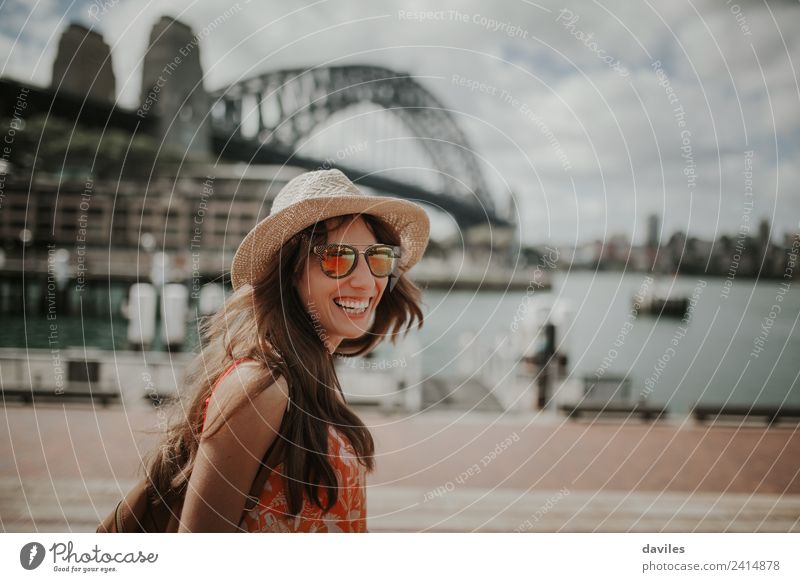 Glückliche blonde Frau mit Hut und Sonnenbrille lacht im Hafen der Stadt Sydney, mit der Harbour Bridge im Hintergrund, in Australien. Lifestyle Stil Freude