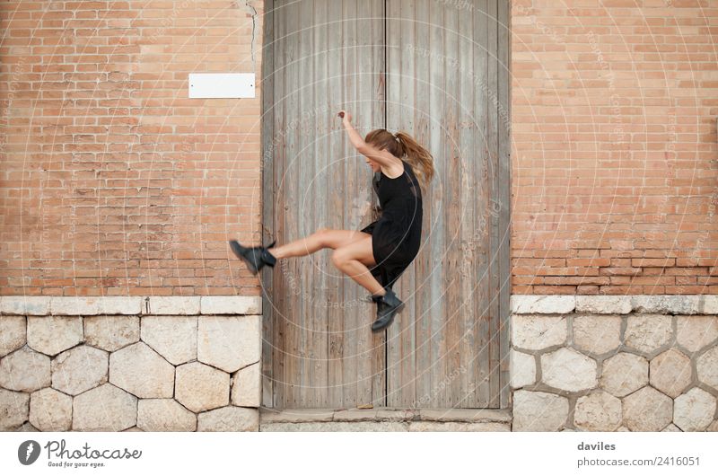 Blonde Frau in schwarzem Kleid tanzt und springt auf der Straße, vor einer alten Hausfassade. elegant Stil Entertainment Tanzen Mensch Junge Frau Jugendliche