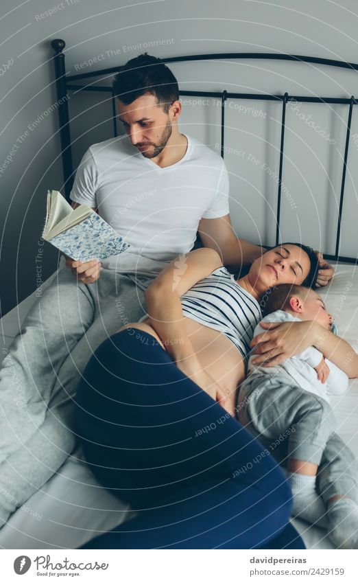 Mann liest mit schwangerer Frau und schlafendem Sohn. schön Erholung lesen Schlafzimmer Kind Mensch Baby Kleinkind Erwachsene Eltern Mutter Vater
