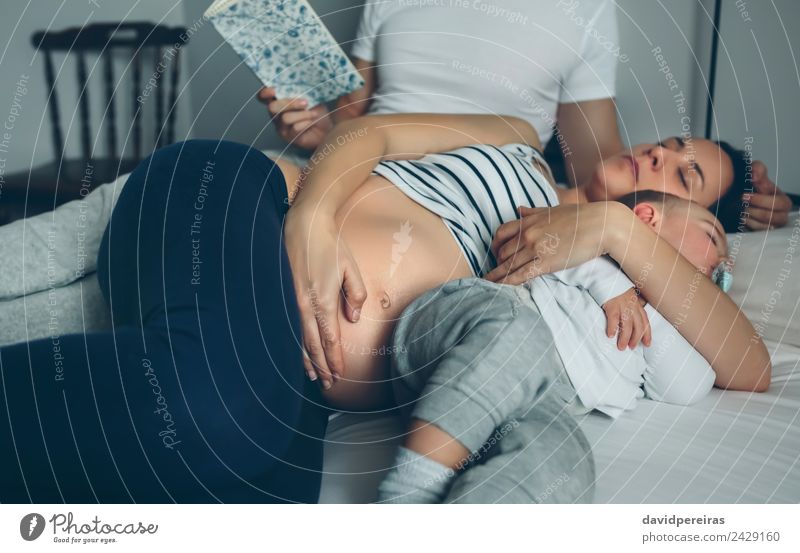 Mann liest mit schwangerer Frau und schlafendem Sohn. schön Erholung lesen Schlafzimmer Kind Mensch Baby Kleinkind Erwachsene Eltern Mutter Vater