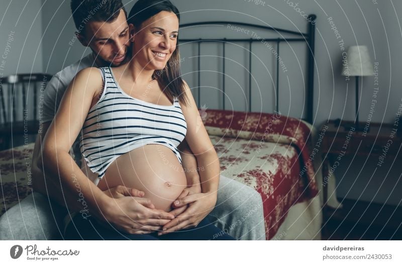 Schwangere Frau, die von ihrem Mann umarmt wird. Schlafzimmer Mensch Baby Erwachsene Eltern Mutter Vater Familie & Verwandtschaft Paar Partner Hand berühren