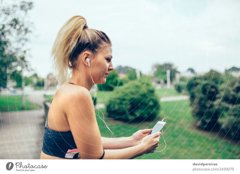 Frau mit Kopfhörer, die Musik auf dem Smartphone hört. Lifestyle schön Sport Joggen Telefon PDA Technik & Technologie Mensch Erwachsene Hand Natur Park blond