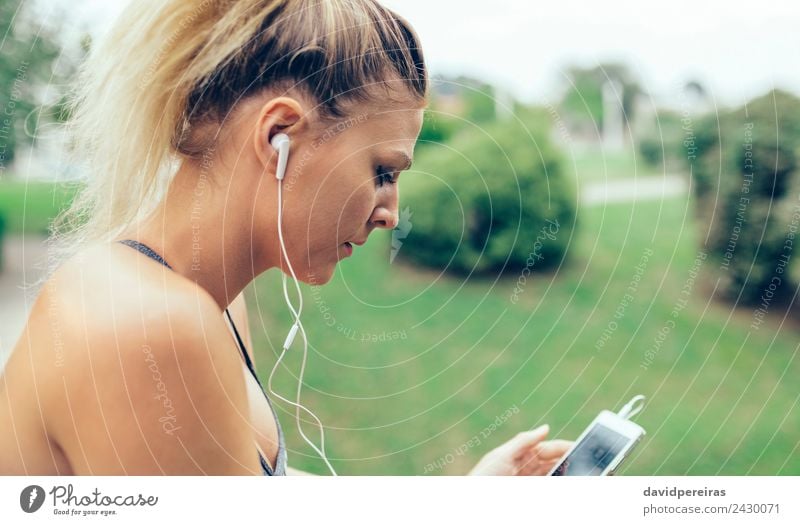 Frau mit Kopfhörer, die Musik auf dem Smartphone hört. Lifestyle Sport Joggen Telefon PDA Technik & Technologie Mensch Erwachsene Hand Park blond Zopf Fitness