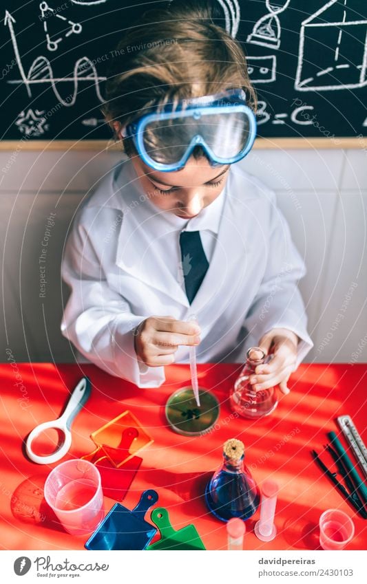Ernsthaftes Kind beim Spielen mit chemischen Flüssigkeiten Flasche Wohnung Tisch Wissenschaften Klassenraum Labor Mensch Junge Kindheit Hand authentisch klein