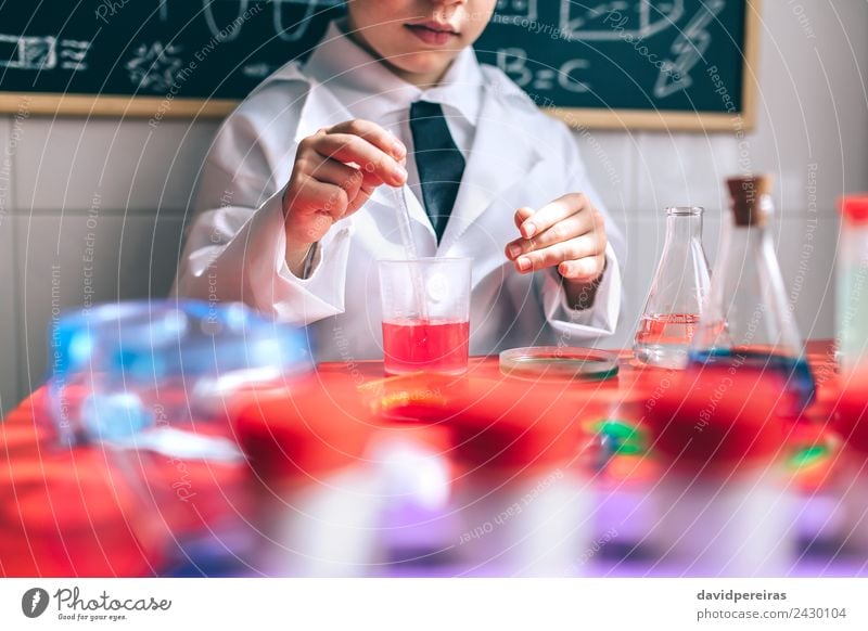 Ein Kind, das spielt, um Chemiker zu werden, mit bunten Flüssigkeiten. Flasche Löffel Spielen Wohnung Tisch Wissenschaften Klassenraum Labor Mensch Junge