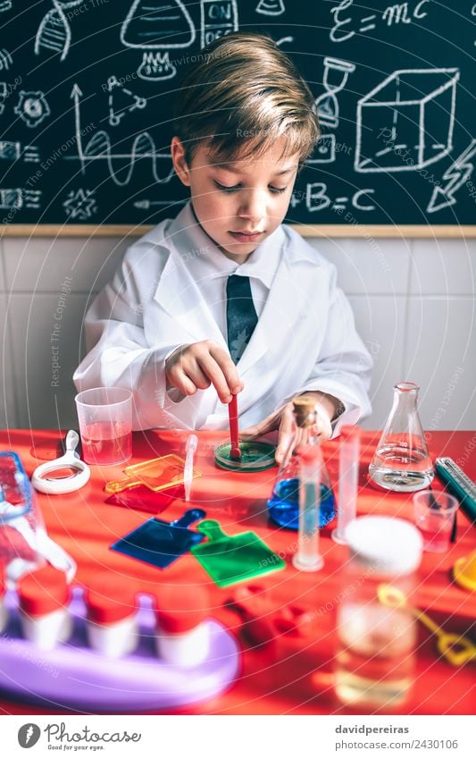 Ein Kind, das spielt, um Chemiker zu werden, mit bunten Flüssigkeiten. Flasche Löffel Glück Spielen Wohnung Tisch Wissenschaften Klassenraum Tafel Labor Mensch