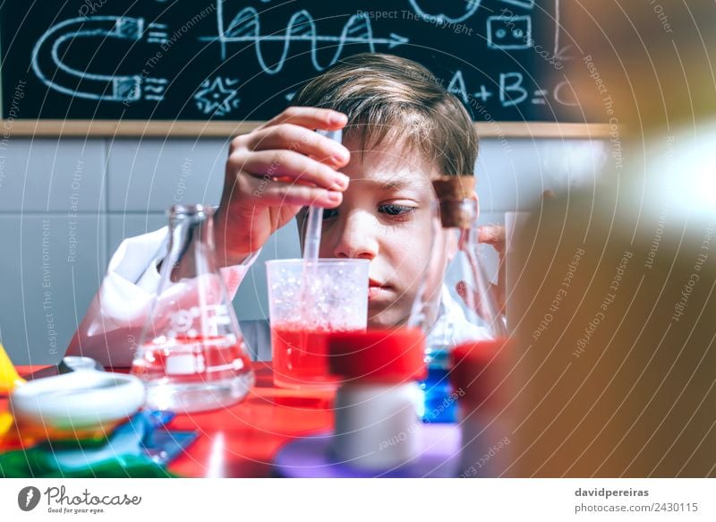 Kind spielt mit chemischen Flüssigkeiten über dem Tisch. Flasche Glück Spielen Wohnung Wissenschaften Klassenraum Tafel Labor Mensch Junge Kindheit Hand