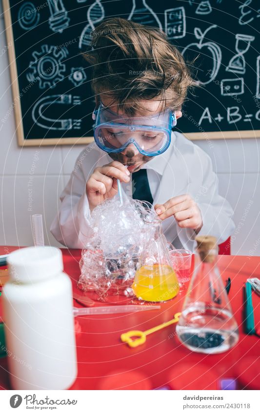 Kind macht Seifenblasen mit Strohhalm im Glas. Gesicht Spielen Wohnung Tisch Wissenschaften Schule Klassenraum Tafel Labor Mensch Junge Kindheit authentisch