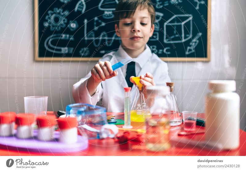 Ernsthafter kleiner Junge beim Spielen mit chemischen Flüssigkeiten Flasche Glück Wohnung Tisch Wissenschaften Kind Klassenraum Tafel Labor Mensch Kindheit Hand