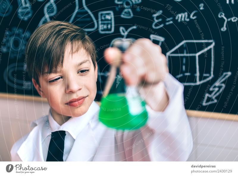 Scientist Kind suchen Kolben mit chemischen grünen Flüssigkeit gegen der Tafel Spielen Wohnung Wissenschaften Klassenraum Labor Mensch Junge Kindheit Mantel