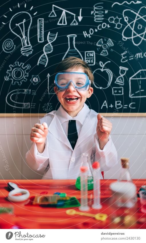 Kleiner Wissenschaftler lachend hinter dem Tisch mit den Experimentierelementen Flasche Glück Spielen Wohnung Wissenschaften Kind Schule Klassenraum Tafel Labor