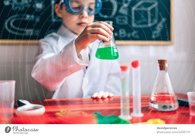 Kleiner Junge Wissenschaftler mit Brille, der eine Flasche gegen eine Tafel hält Spielen Wohnung Tisch Wissenschaften Kind Klassenraum Labor Mensch Kindheit