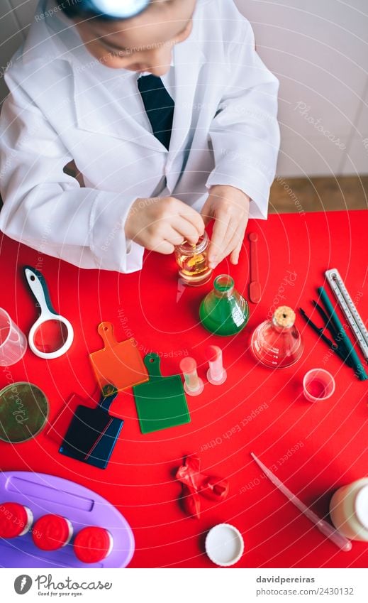 Kleiner Wissenschaftler, der Flüssigkeit in der Flasche mischt. Löffel Spielen Wohnung Tisch Wissenschaften Kind Klassenraum Labor Mensch Junge Kindheit Hand