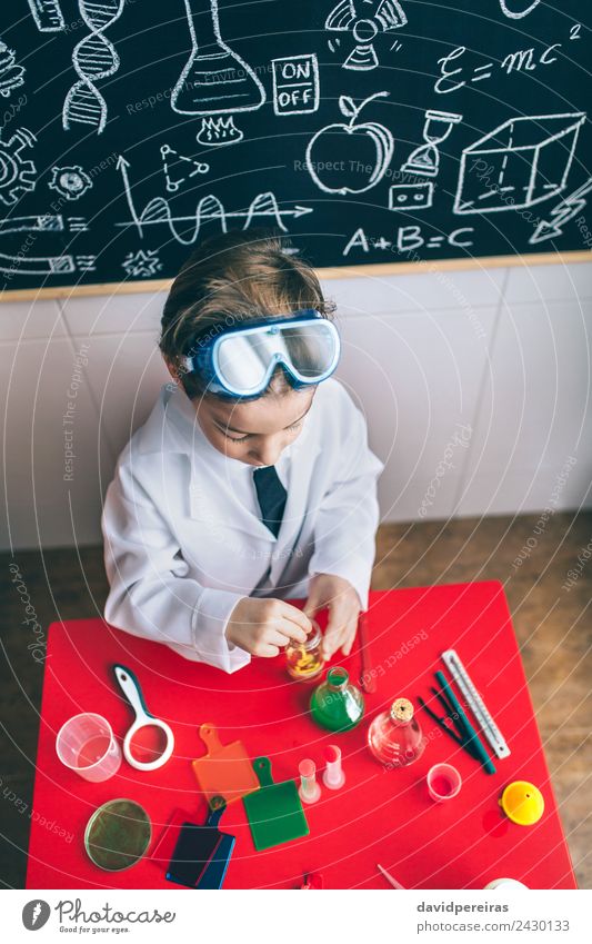 Kind spielt mit chemischen Flüssigkeiten über dem Tisch. Flasche Glück Spielen Wohnung Wissenschaften Klassenraum Tafel Labor Mensch Junge Kindheit Hand
