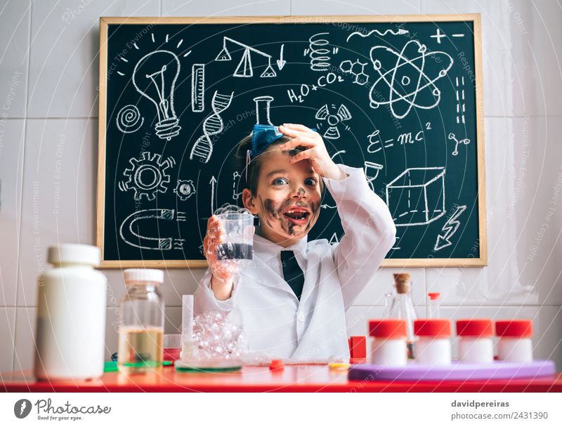 Überrascht kleiner Wissenschaftler mit schmutzigem Gesicht hält Glas mit Seifenschaum Glück Spielen Wohnung Tisch Wissenschaften Kind Schule Klassenraum Tafel