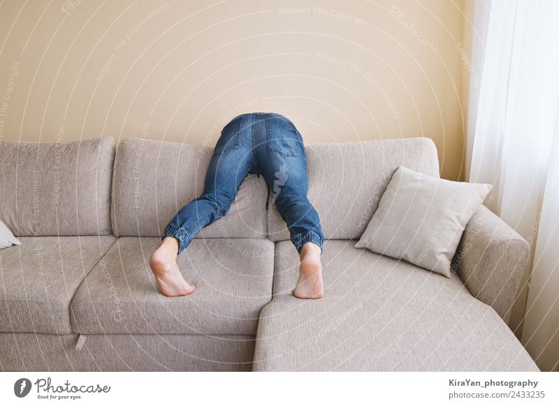 Der Mann in Jeans putzt hinter dem Sofa. Lifestyle Erholung Spielen Möbel Hooligan Erwachsene Vater Gesäß Fuß Bekleidung Jeanshose Traurigkeit Sauberkeit Stress