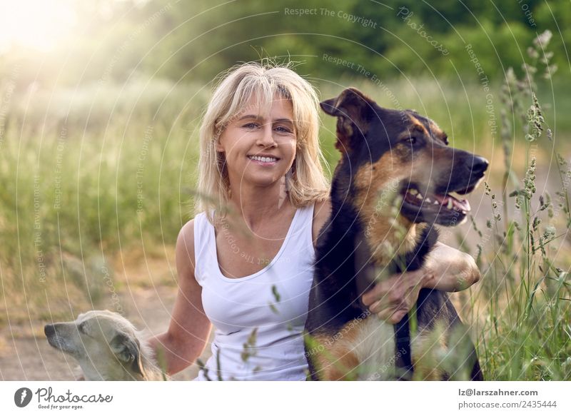 Hübsche blonde Frau mit ihren beiden Hunden. Glück Gesicht Sommer Erwachsene Freundschaft 1 Mensch 45-60 Jahre Tier Gras Wiese Haustier Lächeln Liebe sitzen